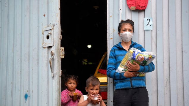 Une femme et deux enfants devant leur maison.