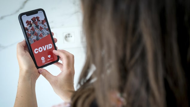 L'image du coronavirus apparaît sur l'écran d'un téléphone intelligent que tient dans ses mains une femme vue de dos.