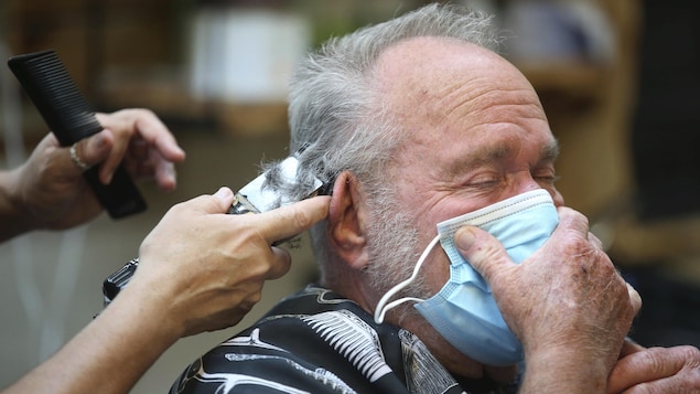 Un homme se fait couper les cheveux en tenant un masque sur son visage.