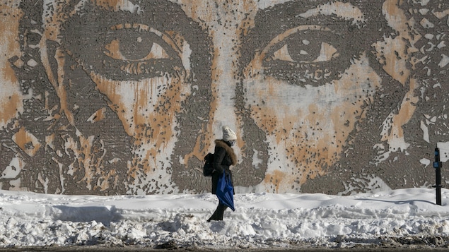 Une femme marche dans la neige devant une grande murale.