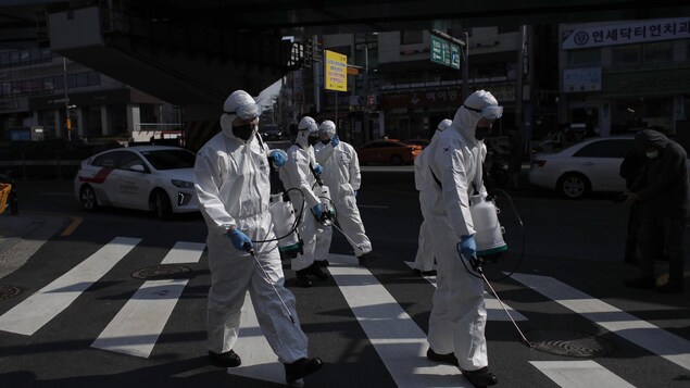 Des soldats envoient du désinfectant dans les rues en Corée du Sud. Ils sont habillés de blanc et portent des masques.