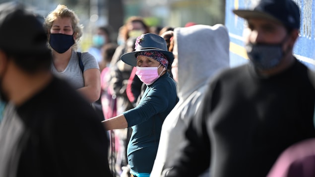 Une foule de gens masqués autour d'une dame âgée.