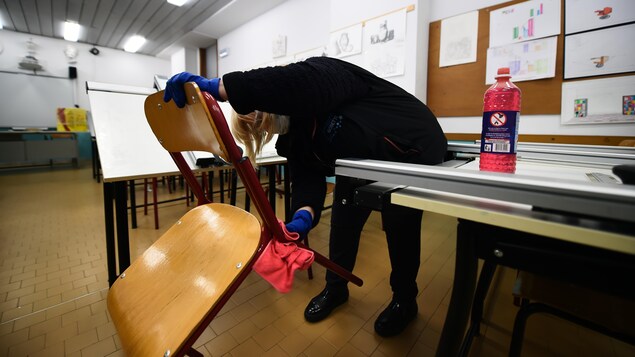 Une femme portant des gants nettoie les pattes d'une chaise dans une salle de classe.