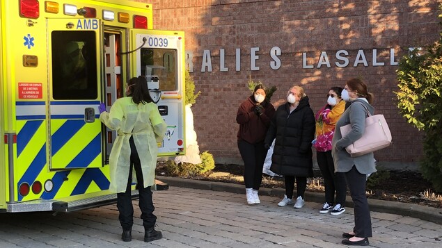 Quatre femmes regardent en direction d'une ambulance dont les portes sont entrain d'être fermées par le personnel médical.
