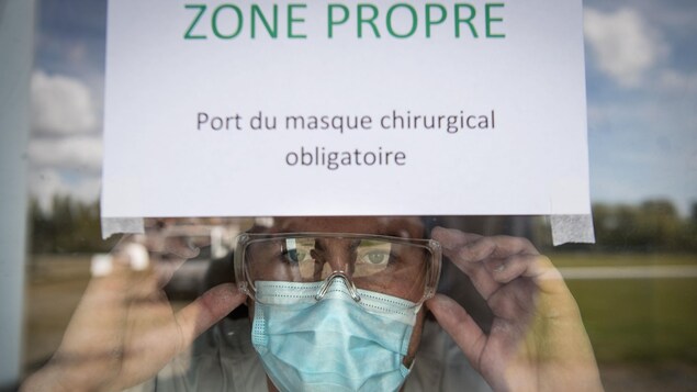 Un travailleur de la santé français derrière une fenêtre sur laquelle une affiche est collée indiquant une «Zone propre».