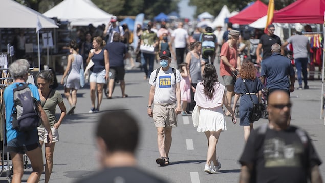 Un homme portant un masque marche sur le boulevard Saint-Laurent, à Montréal, au milieu d'une foule de piétons.