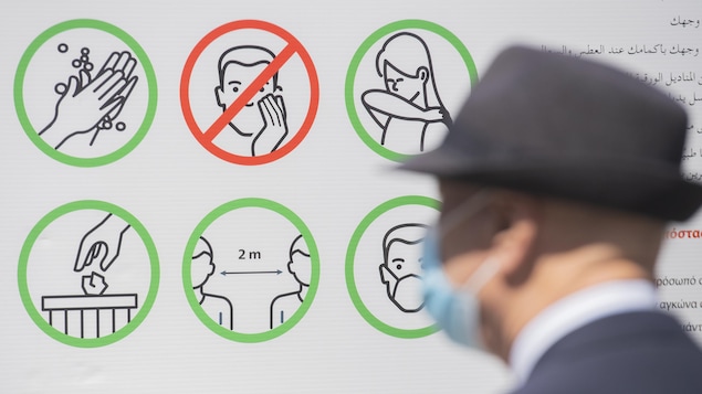 Un homme passe devant une illustration rappelant les règles sanitaires, comme le lavage de mains et la distanciation.