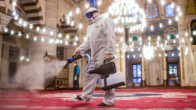 Un homme en combinaison de protection pulvérise du désinfectant sur un tapis.