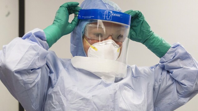 Une employée portant une visière, un masque et des gants.