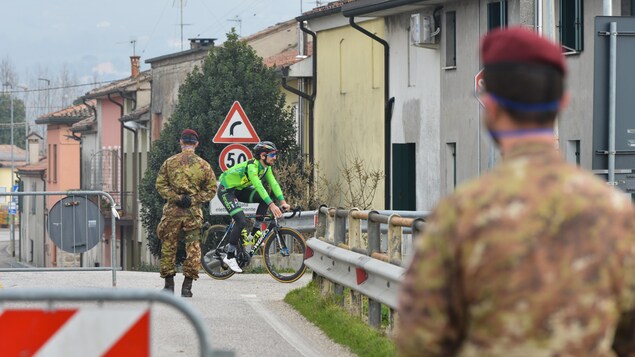Un vélo pédale alors que deux soldats contrôlent un point d'entrée.