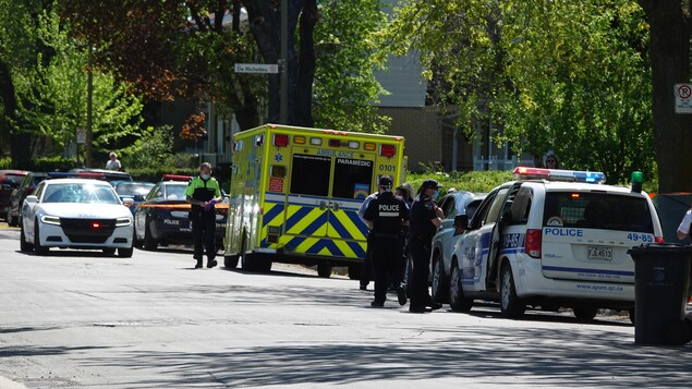 Des voitures de police et une ambulance dans une rue au périmètre sécurisé.