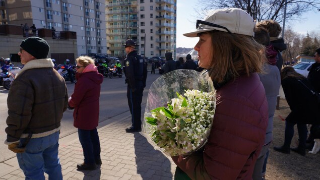 Une jeune femme tient un bouquet de fleurs en regardant la procession funéraire.