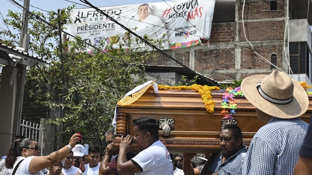 Une femme asperge un cercueil porté par des hommes dans une rue, devant une banderole électorale d'Alfredo Carbrera, le défunt.