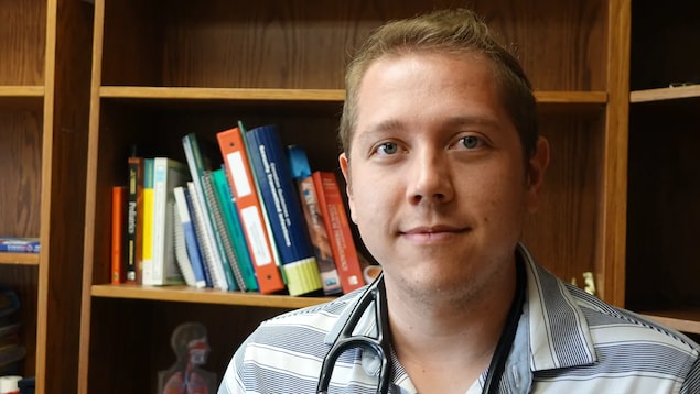 Le Dr Cory Scott pose pour la caméra dans un bureau de médecin.