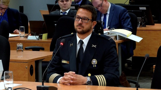 Un homme portant des lunettes rectangulaires et un uniforme noir avec des reliefs beige ou or et un insigne du SPVM à gauche, regarde droit devant lui.