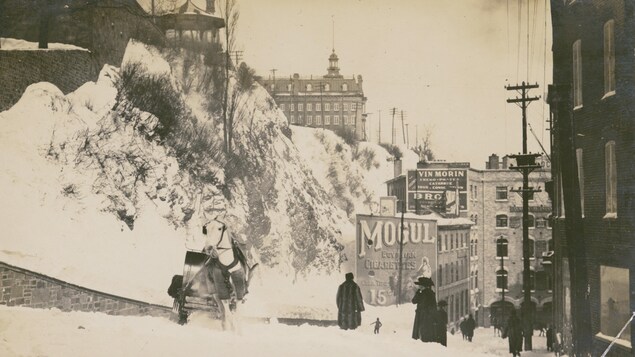 Des passants arpentent la côte de la Montagne, l'une des plus raides de la capitale. Une dame élégante se mouche au premier plan, près d'un cheval qui fait voler la neige autour de lui.