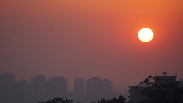 Un coucher de soleil avec un écran de fumée avec des immeubles en arrière plan.