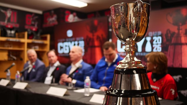 Des autorités du sport sont assis à une table en arrière-plan, derrière la Coupe Grey au premier plan, lors de l'annonce de Calgary comme ville hôte en 2026, le 8 novembre 2024.