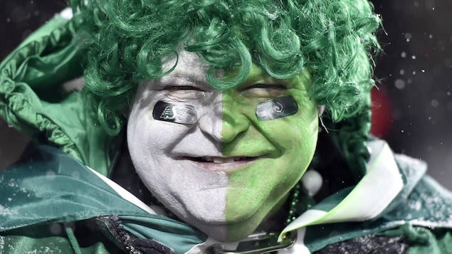 Un homme vêtu de vert et dont le visage est peint en vert et blanc sourit. Un homme vêtu de vert et dont le visage est peint en vert et blanc sourit.