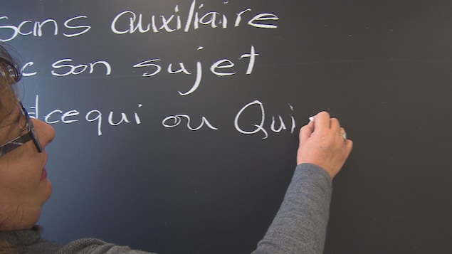 Une femme explique la grammaire française en écrivant sur une ardoise à l'aide d'une craie.