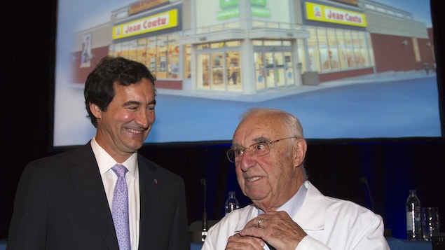 François J. Coutu et son père Jean Coutu devant une affiche d'un magasin François J. Coutu et son père Jean Coutu devant une affiche d'un magasin