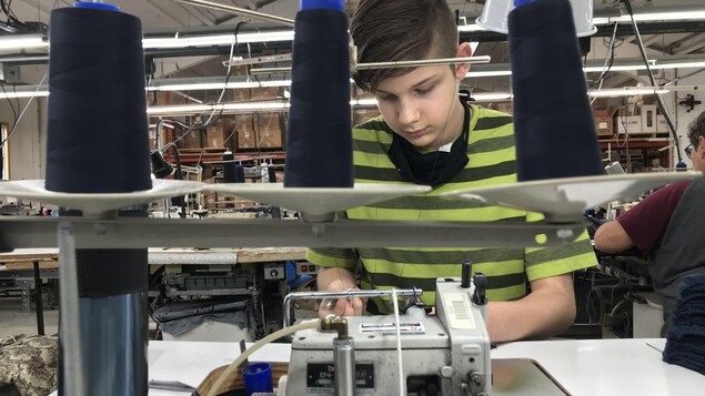 Un jeune garçon se concentre à faire des masques sur une machine à coudre.