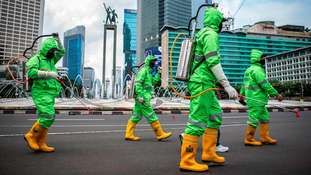 Des travailleurs marchent en combinaison de protection lors d'une opération de pulvérisation de désinfectant pour prévenir la propagation de la COVID-19 à Jakarta, la capitale de l’Indonésie.