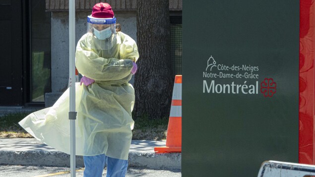 Une travailleuse de la santé, en équipement de protection, attend la tête baissée près de l'aréna.