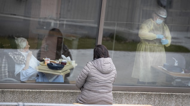 Une femme observe par la fenêtre d'un CHSLD une patiente qui attend qu'une préposée, revêtant un équipement de protection et un masque, lui serve un repas.

Photo prise  au CHSLD Éloria Lepage à  Montréal,  Québec, Canada.

Sur la photo: (Gauche à droite) Chantal Grenier (de dos) est venu voir sa mère de 90 ans, Anita Roy (qui est atteinte du Covid19) (avec son conjoint, Roger Comptois de dos)

Le 26 Avril, 2020    2020/04/26