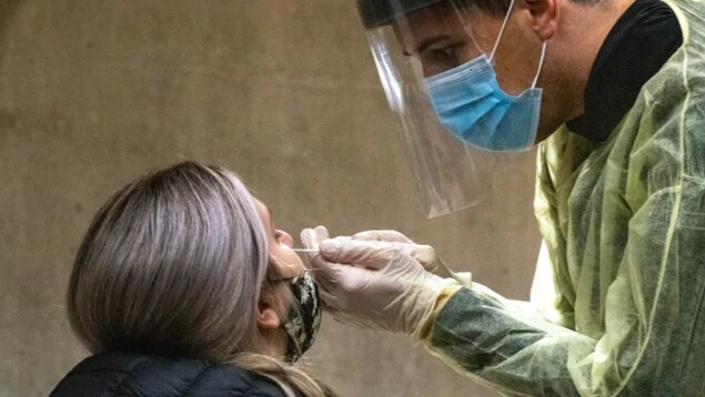 Un homme fait un prélèvement sur une femme dans le cadre d'un test de dépistage de la COVID-19.