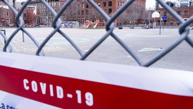 Une affiche disant COVID-19 sur la clôture d'une cour d'école fermée à Montréal.