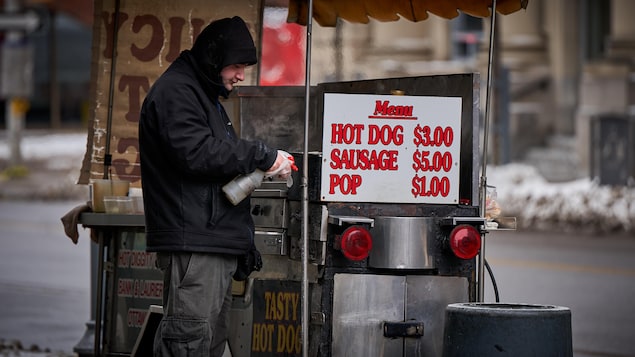 Un homme désinfecte son kiosque à hot-dogs, à l'extérieur.