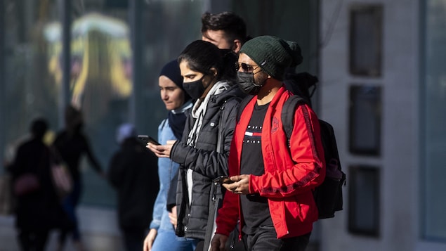 Des gens portant des masques marchent le long de la rue Granville, à Vancouver.