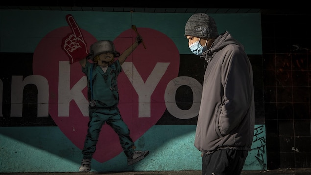 Une personne portant un masque marche devant une murale au centre-ville de Vancouver.  