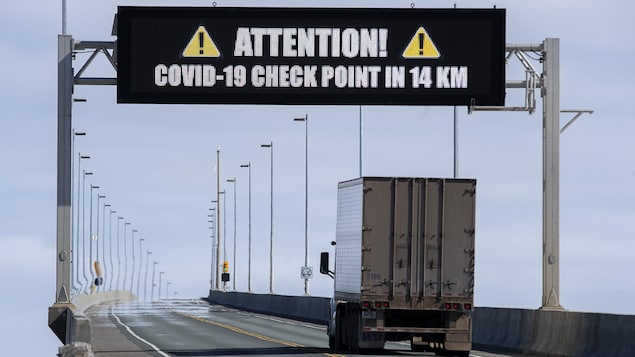 Un camion lourd passe sous le tableau numérique du pont, qui annonce un point de contrôle de la COVID-19 dans 14 kilomètres.
