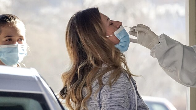 
A swab enters the nostril of a woman wearing a blue mask over her mouth.