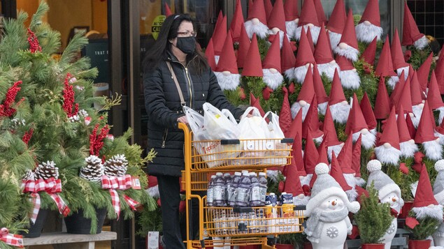 Une cliente sort de l'épicerie avec un panier rempli de provisions.
