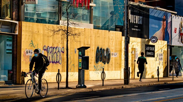 Un cycliste devant des commerces dont la devanture est recouverte de planches de bois.
