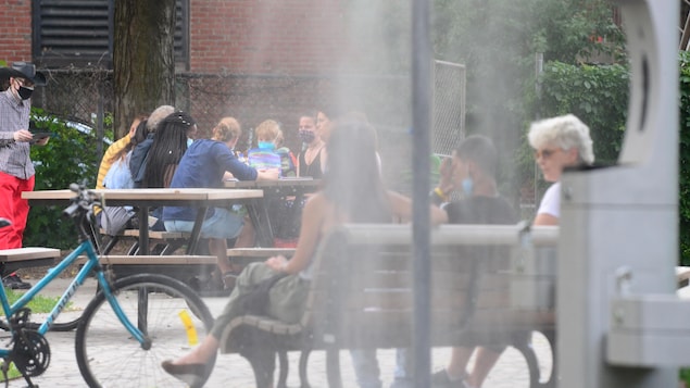 Des jeunes sont assis à une table dehors tandis que des personnes plus âgées sont sur un banc.