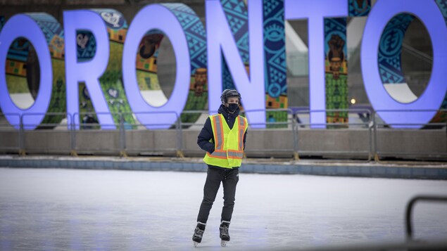 Un homme en patins sur une patinoire devant les lettres lumineuses de Toronto.