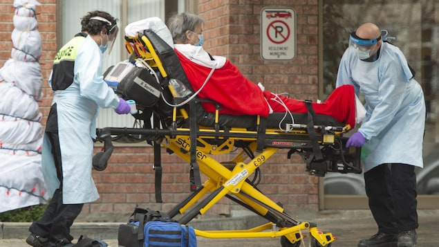 Une patiente aînée transportée sur une civière par des ambulanciers.