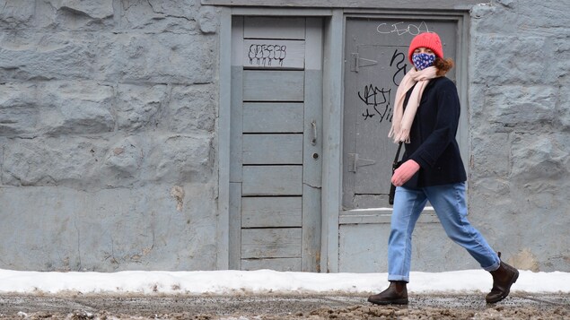 Une femme masquée marche sur le trottoir.
