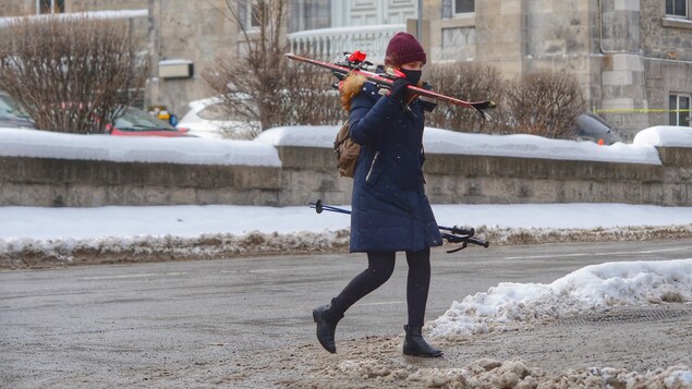 Une femme transporte des skis alpins en marchant dans la rue.