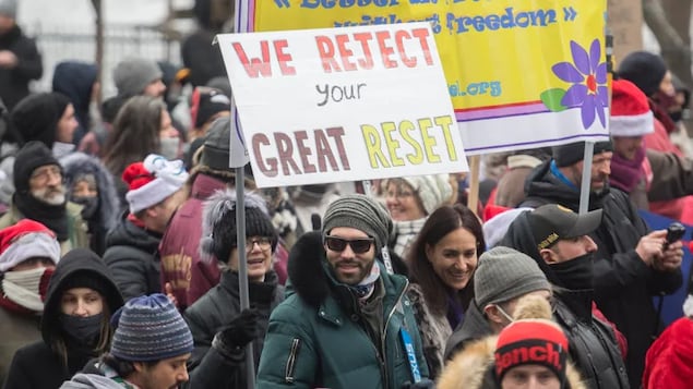 People participate in a demonstration in Montreal protesting measures implemented by the Quebec government to help stop the spread of COVID-19 on December 20, 2020. One protester holds a sign referring to the 'Great Reset' conspiracy theory. (Graham Hughes/The Canadian Press)