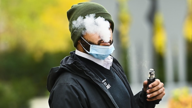 Un homme abaisse son masque pour fumer avec une vapoteuse.