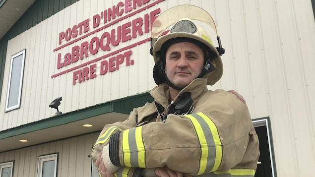Un homme en uniforme de pompier se tient debout devant le poste d'incendie de La Broquerie.