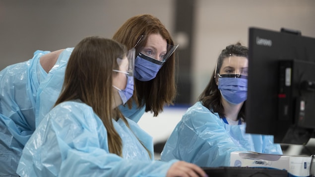 Trois travailleuses de la santé portant des masques regardent un écran d'ordinateur.