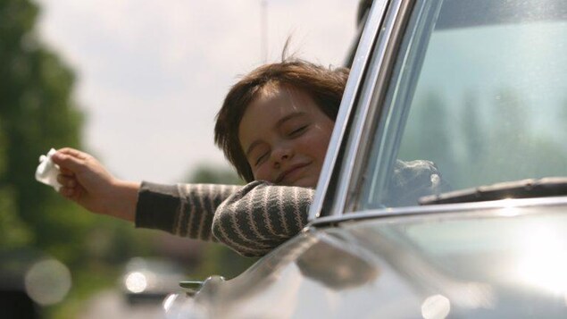 Le jeune garçon tient un mouchoir dans sa main alors qu'il passe la tête dans l'ouverture d'une vitre d'auto.