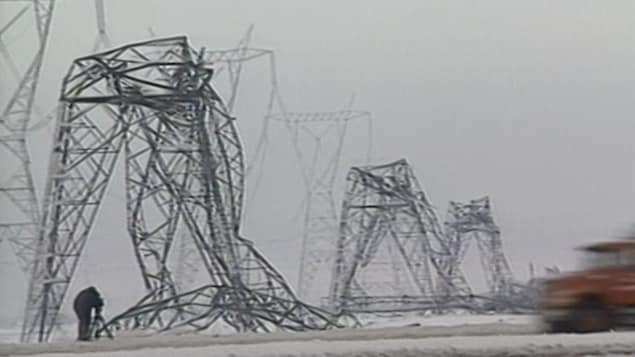 Un caméraman filme une rangée de pylônes électriques en acier pliés en deux sous le poids de la glace.