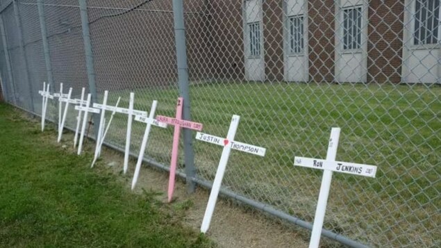 Des croix en bois posées contre le grillage d'une prison.